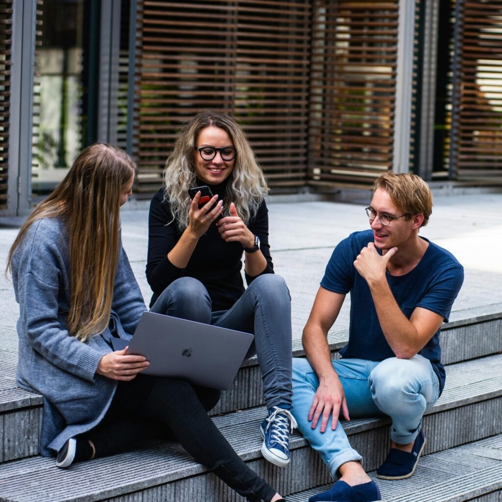 Three young professionals having a friendly chat while sitting on outdoor steps.