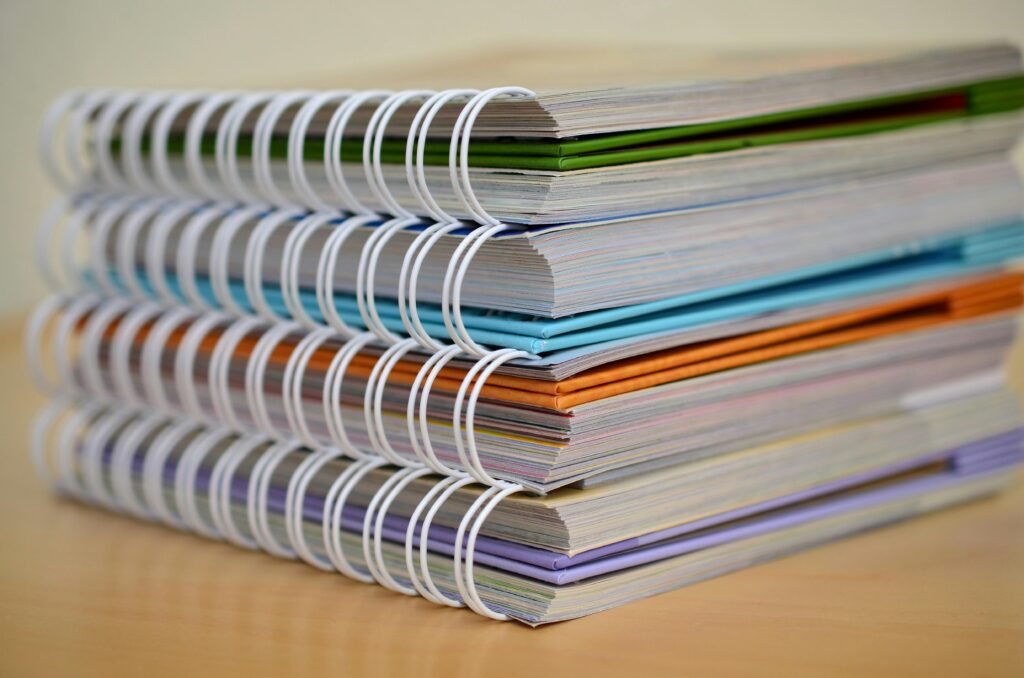 pexels-photo-272980-272980 A colorful stack of spiral-bound notebooks neatly placed on a wooden desk. Ideal for educational themes.