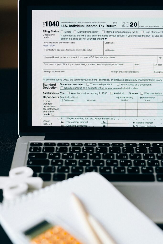pexels-photo-6863246-6863246 Close-up of a tax form on a laptop screen with a calculator and notebook in the foreground.
